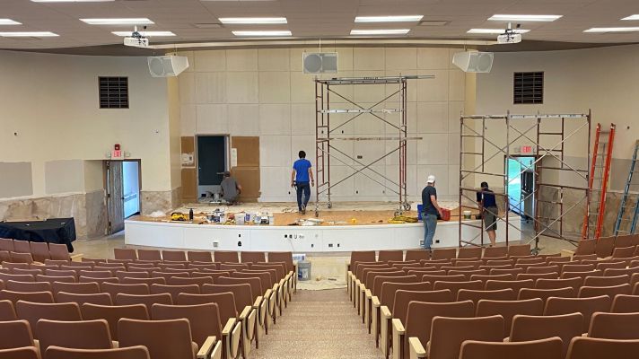 Auditorium with renovation in progress; men working, scaffolding, and ladders.