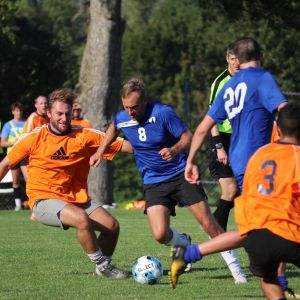 Alumni playing soccer in blue and orange jerseys