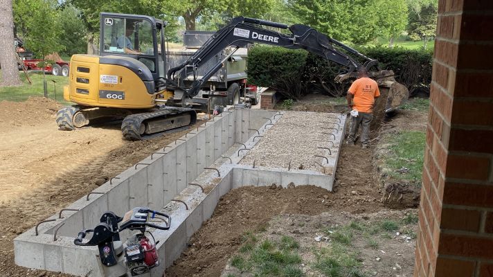 Excavator next to concrete trench with men working outside building